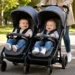 Passeggino gemellare con due bambini durante una passeggiata in un parco alberato.