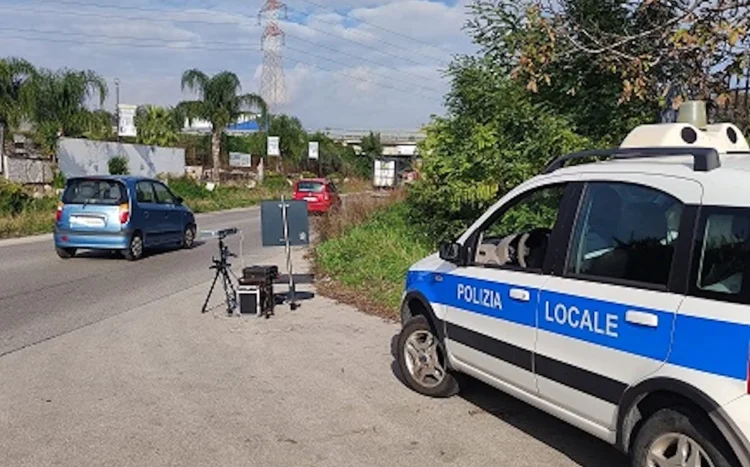 Postazione autovelox mobile della Polizia Locale con apparecchiatura su treppiede e pattuglia ferma a bordo strada
