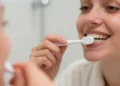 persona adulta che si lava i denti davanti allo specchio, con luce naturale e focus su spazzolino e gengive sane.
