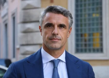 Oggi questa foto da migliorare a corredo di questo articolo [La politica vittoriese vive ore di fortissima attesa. Il nome di Salvo Sallemi è balzato in pole position per la guida del Ministero del Turismo. La poltrona di Daniela Santanchè a via Villa Ada è ufficialmente vuota. La premier Giorgia Meloni accelera ora per definire la successione. Tra i profili più accreditati emerge con forza quello del senatore ibleo. L'esponente di Fratelli d'Italia rappresenta infatti una figura chiave per l'equilibrio della maggioranza di governo. Sallemi a La Sicilia: "Contento che il mio partito mi consideri" Il senatore di Vittoria mantiene un profilo istituzionale e cauto. "Non ho saputo nulla fino adesso", dichiara Sallemi in un'intervista rilasciata al quotidiano La Sicilia. "Ma sono contento di essere stato inserito in questo totonomi", aggiunge con pragmatismo. Egli si definisce un militante storico sempre a disposizione del proprio partito. La sua fedeltà alla linea di Palazzo Chigi appare incrollabile in questa delicata fase di rimpasto. Salvo Sallemi: il volto di Vittoria a Roma L'avvocato quarantanovenne siede a Palazzo Madama dal 2022. Sallemi ha lavorato intensamente nelle commissioni Giustizia e Antimafia. La sua nomina garantirebbe un raccordo fondamentale con le istanze del Sud Italia. Il senatore proviene dal ragusano, un’area che vive una crescita turistica senza precedenti. La sua esperienza territoriale compenserebbe la mancanza di incarichi specifici nel settore. Classe 1977, Sallemi siede al Senato dal 2022. La sua ascesa politica riflette una militanza storica e coerente tra le fila di Fratelli d'Italia. A Roma, il senatore ha saputo distinguersi per il suo impegno costante. Egli opera infatti all'interno delle prestigiose commissioni Giustizia e Antimafia. In questi contesti, Sallemi ha dimostrato una preparazione tecnica e giuridica di alto livello. Un ponte tra il Governo e le istanze del Sud L'eventuale nomina ministeriale di Sallemi garantirebbe un raccordo diretto con il Meridione. Il Governo Meloni troverebbe in lui un interprete autentico delle necessità siciliane. Sallemi incarna la voce di un territorio che chiede infrastrutture e sviluppo. La sua presenza nell'esecutivo sarebbe un segnale di forte attenzione verso l'Isola. Egli conosce profondamente le dinamiche dello sviluppo locale e delle piccole medie imprese. Il "modello Ragusa" come biglietto da visita Il senatore proviene da un’area geografica simbolo del riscatto turistico siciliano. Sebbene Sallemi non vanti incarichi tecnici pregressi nel turismo, la sua forza risiede proprio qui. Egli porta con sé l'esperienza di chi ha visto trasformare la propria terra. Dalla professione forense alla sfida ministeriale La carriera di Salvo Sallemi affonda le radici nella professione legale. Questo background gli conferisce una rara capacità di analisi delle norme complesse. Da avvocato a senatore, il passo è stato segnato dal consenso dei cittadini iblei. Oggi, la sfida del Ministero del Turismo appare come il coronamento di un lungo percorso. Per Vittoria e per l'intera provincia di Ragusa, avere un proprio esponente in via Villa Ada sarebbe un evento storico.] mi serve titolo, alt text, didascalia, descrizione Ecco un set completo e professionale di titolo, alt text, didascalia e descrizione per accompagnare l’articolo e la foto che hai caricato. Li ho formulati in stile editoriale, neutro e istituzionale, perfetti per un quotidiano online. 📰 Titolo suggerito Salvo Sallemi in pole position per il Ministero del Turismo: cresce l’attesa a Vittoria 🖼️ Alt text (accessibilità) Ritratto del senatore Salvo Sallemi in abito formale, fotografato all’esterno di un edificio istituzionale.