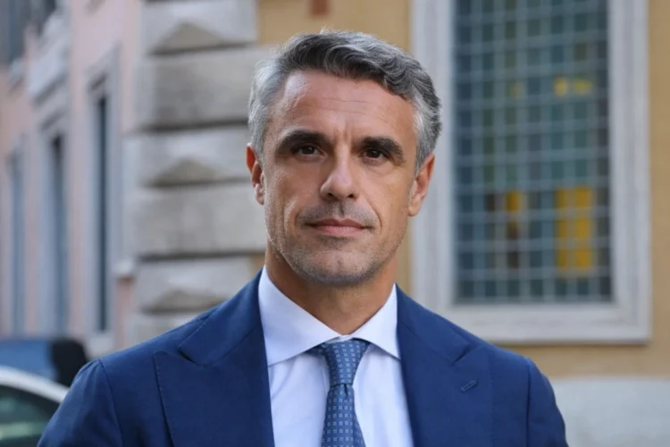 Oggi questa foto da migliorare a corredo di questo articolo [La politica vittoriese vive ore di fortissima attesa. Il nome di Salvo Sallemi è balzato in pole position per la guida del Ministero del Turismo. La poltrona di Daniela Santanchè a via Villa Ada è ufficialmente vuota. La premier Giorgia Meloni accelera ora per definire la successione. Tra i profili più accreditati emerge con forza quello del senatore ibleo. L'esponente di Fratelli d'Italia rappresenta infatti una figura chiave per l'equilibrio della maggioranza di governo. Sallemi a La Sicilia: "Contento che il mio partito mi consideri" Il senatore di Vittoria mantiene un profilo istituzionale e cauto. "Non ho saputo nulla fino adesso", dichiara Sallemi in un'intervista rilasciata al quotidiano La Sicilia. "Ma sono contento di essere stato inserito in questo totonomi", aggiunge con pragmatismo. Egli si definisce un militante storico sempre a disposizione del proprio partito. La sua fedeltà alla linea di Palazzo Chigi appare incrollabile in questa delicata fase di rimpasto. Salvo Sallemi: il volto di Vittoria a Roma L'avvocato quarantanovenne siede a Palazzo Madama dal 2022. Sallemi ha lavorato intensamente nelle commissioni Giustizia e Antimafia. La sua nomina garantirebbe un raccordo fondamentale con le istanze del Sud Italia. Il senatore proviene dal ragusano, un’area che vive una crescita turistica senza precedenti. La sua esperienza territoriale compenserebbe la mancanza di incarichi specifici nel settore. Classe 1977, Sallemi siede al Senato dal 2022. La sua ascesa politica riflette una militanza storica e coerente tra le fila di Fratelli d'Italia. A Roma, il senatore ha saputo distinguersi per il suo impegno costante. Egli opera infatti all'interno delle prestigiose commissioni Giustizia e Antimafia. In questi contesti, Sallemi ha dimostrato una preparazione tecnica e giuridica di alto livello. Un ponte tra il Governo e le istanze del Sud L'eventuale nomina ministeriale di Sallemi garantirebbe un raccordo diretto con il Meridione. Il Governo Meloni troverebbe in lui un interprete autentico delle necessità siciliane. Sallemi incarna la voce di un territorio che chiede infrastrutture e sviluppo. La sua presenza nell'esecutivo sarebbe un segnale di forte attenzione verso l'Isola. Egli conosce profondamente le dinamiche dello sviluppo locale e delle piccole medie imprese. Il "modello Ragusa" come biglietto da visita Il senatore proviene da un’area geografica simbolo del riscatto turistico siciliano. Sebbene Sallemi non vanti incarichi tecnici pregressi nel turismo, la sua forza risiede proprio qui. Egli porta con sé l'esperienza di chi ha visto trasformare la propria terra. Dalla professione forense alla sfida ministeriale La carriera di Salvo Sallemi affonda le radici nella professione legale. Questo background gli conferisce una rara capacità di analisi delle norme complesse. Da avvocato a senatore, il passo è stato segnato dal consenso dei cittadini iblei. Oggi, la sfida del Ministero del Turismo appare come il coronamento di un lungo percorso. Per Vittoria e per l'intera provincia di Ragusa, avere un proprio esponente in via Villa Ada sarebbe un evento storico.] mi serve titolo, alt text, didascalia, descrizione Ecco un set completo e professionale di titolo, alt text, didascalia e descrizione per accompagnare l’articolo e la foto che hai caricato. Li ho formulati in stile editoriale, neutro e istituzionale, perfetti per un quotidiano online. 📰 Titolo suggerito Salvo Sallemi in pole position per il Ministero del Turismo: cresce l’attesa a Vittoria 🖼️ Alt text (accessibilità) Ritratto del senatore Salvo Sallemi in abito formale, fotografato all’esterno di un edificio istituzionale.