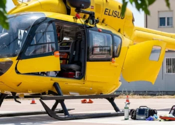Fotografia ravvicinata dell'elicottero giallo del 118 "ELISUD" con il portellone aperto, attrezzature mediche (monitor, zaino, ossigeno) a terra sulla piazzola dell'Ospedale Maggiore di Modica.