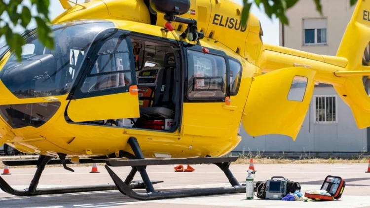Fotografia ravvicinata dell'elicottero giallo del 118 "ELISUD" con il portellone aperto, attrezzature mediche (monitor, zaino, ossigeno) a terra sulla piazzola dell'Ospedale Maggiore di Modica.