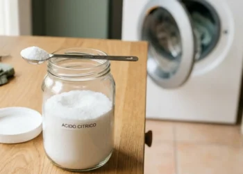Barattolo di acido citrico in polvere con cucchiaio dosatore su piano cucina, utilizzato come decalcificante naturale per lavatrice