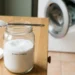 Barattolo di acido citrico in polvere con cucchiaio dosatore su piano cucina, utilizzato come decalcificante naturale per lavatrice