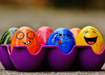 Biglietto d'auguri con la scritta Buona Pasqua 2026 circondato da uova colorate e fiori primaverili.