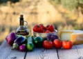 Vista aerea di una tavola mediterranea rustica in campagna siciliana con olio extravergine d’oliva, pomodori di Pachino, formaggio Ragusano e verdure di stagione