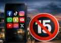 Uno smartphone con icone social e un segnale di divieto per rappresentare il limite dei social network ai minori di 15 anni.