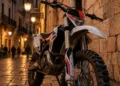 Moto da cross ferma su strada acciottolata in un centro storico siciliano di sera — immagine illustrativa generata con IA