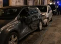 Immagine generata con IA che raffigura una strada urbana con auto danneggiata e posto di controllo delle forze dell’ordine, senza persone identificabili.
