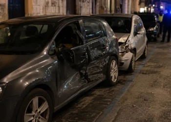 Immagine generata con IA che raffigura una strada urbana con auto danneggiata e posto di controllo delle forze dell’ordine, senza persone identificabili.