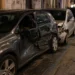Immagine generata con IA che raffigura una strada urbana con auto danneggiata e posto di controllo delle forze dell’ordine, senza persone identificabili.