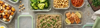 Contenitori in vetro per il meal prep con broccoli, quinoa, salmone, ceci, uova sode e frutti di bosco su sfondo in pietra, ideali per una dieta dimagrante equilibrata e organizzata.