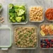 Contenitori in vetro per il meal prep con broccoli, quinoa, salmone, ceci, uova sode e frutti di bosco su sfondo in pietra, ideali per una dieta dimagrante equilibrata e organizzata.