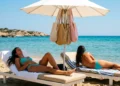 Due persone si rilassano su lettini sotto un ombrellone sulla spiaggia sabbiosa di Marina di Modica, con borse appese.