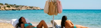 Due persone si rilassano su lettini sotto un ombrellone sulla spiaggia sabbiosa di Marina di Modica, con borse appese.