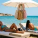 Due persone si rilassano su lettini sotto un ombrellone sulla spiaggia sabbiosa di Marina di Modica, con borse appese.