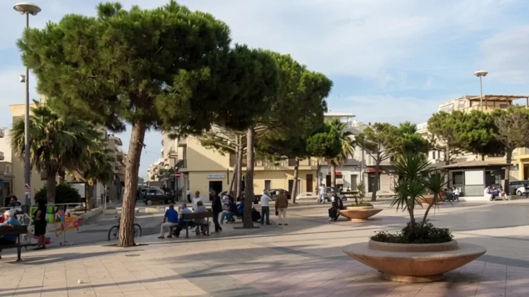 Veduta di piazza Cavour a Scoglitti con alberi, panchine e persone presenti nell'area urbana durante il giorno