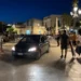 Auto all'interno di un'area pedonale affollata durante le ore serali, con cittadini che osservano la scena in una piazza di Marina di Ragusa