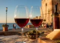 Immagine editoriale generata con intelligenza artificiale: calici di vino rosso Cerasuolo su tavolo con prodotti tipici siciliani, sullo sfondo la Torre Cabrera e il mare di Pozzallo durante la rassegna Calici dei Cabrera