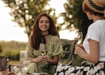 Due donne con abiti estivi sorseggiano un aperitivo all'aperto durante una serata estiva, con look leggeri e informali