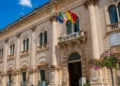 Facciata del Palazzo Municipale di Scicli, sede del Comune, con le bandiere italiana, europea e siciliana all'ingresso.