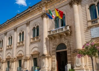 Facciata del Palazzo Municipale di Scicli, sede del Comune, con le bandiere italiana, europea e siciliana all'ingresso.