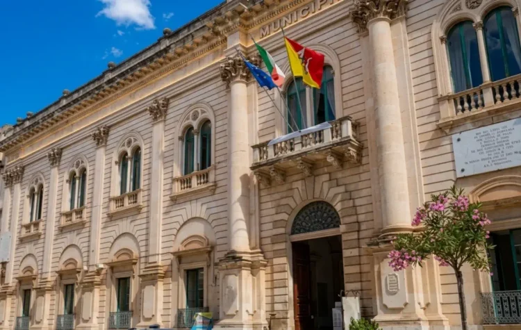 Facciata del Palazzo Municipale di Scicli, sede del Comune, con le bandiere italiana, europea e siciliana all'ingresso.