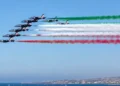 Frecce Tricolori in formazione sul mare durante un sorvolo con scie verde, bianca e rossa.