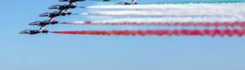 Frecce Tricolori in formazione sul mare durante un sorvolo con scie verde, bianca e rossa.
