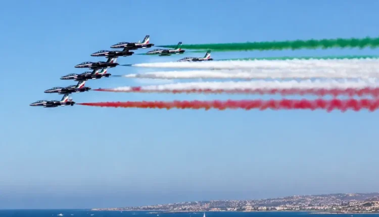Frecce Tricolori in formazione sul mare durante un sorvolo con scie verde, bianca e rossa.