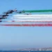 Frecce Tricolori in formazione sul mare durante un sorvolo con scie verde, bianca e rossa.