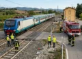 Treno regionale fermo sui binari vicino a un furgone danneggiato con cisterna a un passaggio a livello.