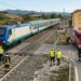 Treno regionale fermo sui binari vicino a un furgone danneggiato con cisterna a un passaggio a livello.