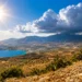 Panorama della Sicilia sotto un sole intenso con cielo in prevalenza sereno, nubi temporalesche in formazione sui rilievi interni e un grande termometro che indica temperature vicine ai 38°C, simbolo dell'ondata di caldo estivo