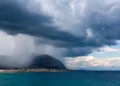 Panorama della costa siciliana con nubi temporalesche e pioggia in avvicinamento sul mare e sulle montagne.