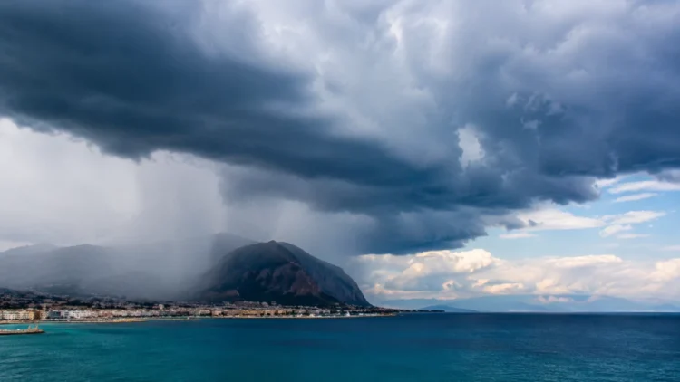 Panorama della costa siciliana con nubi temporalesche e pioggia in avvicinamento sul mare e sulle montagne.