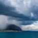 Panorama della costa siciliana con nubi temporalesche e pioggia in avvicinamento sul mare e sulle montagne.
