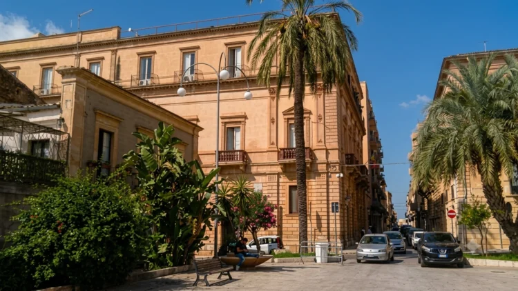 Veduta del centro di Vittoria con edifici storici e palme lungo una strada cittadina