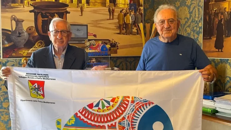 Due rappresentanti locali mostrano la bandiera REIMAR durante un'iniziativa dedicata alle identità marinare siciliane.