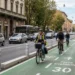 Ciclisti lungo una strada con infrastrutture dedicate alla mobilità sicura e traffico veicolare ordinario.