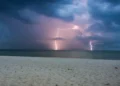 Temporale con fulmini su una città costiera durante la notte, con nubi scure e pioggia intensa. Immagine rappresentativa del peggioramento meteo previsto in Sicilia con calo delle temperature e possibili precipitazioni da inizio luglio.
