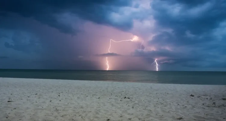 Temporale con fulmini su una città costiera durante la notte, con nubi scure e pioggia intensa. Immagine rappresentativa del peggioramento meteo previsto in Sicilia con calo delle temperature e possibili precipitazioni da inizio luglio.