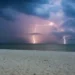 Temporale con fulmini su una città costiera durante la notte, con nubi scure e pioggia intensa. Immagine rappresentativa del peggioramento meteo previsto in Sicilia con calo delle temperature e possibili precipitazioni da inizio luglio.