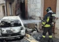 Un Vigile del Fuoco interviene per spegnere l'auto completamente distrutta dalle fiamme in via Rattazzi a Vittoria, dove il rogo ha danneggiato anche il portone di un'abitazione