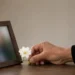 Una mano depone un fiore bianco accanto a una fotografia sfocata su uno sfondo neutro, simbolo delle donazioni in memoria e della solidarietà verso chi vive emergenze umanitarie