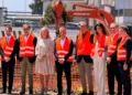 I rappresentanti di Sibeg Coca-Cola, delle istituzioni e dei partner industriali durante la posa della prima pietra del nuovo polo logistico automatizzato nello stabilimento di Catania, con un escavatore sullo sfondo.