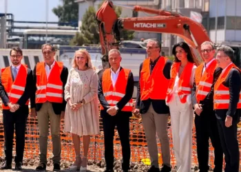 I rappresentanti di Sibeg Coca-Cola, delle istituzioni e dei partner industriali durante la posa della prima pietra del nuovo polo logistico automatizzato nello stabilimento di Catania, con un escavatore sullo sfondo.