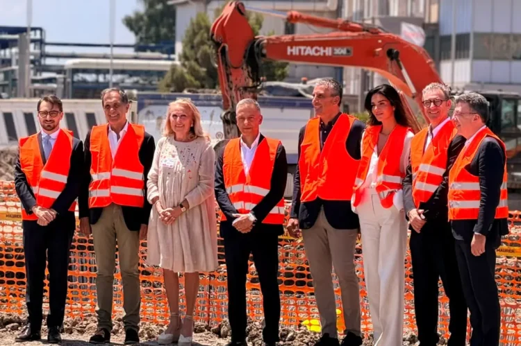 I rappresentanti di Sibeg Coca-Cola, delle istituzioni e dei partner industriali durante la posa della prima pietra del nuovo polo logistico automatizzato nello stabilimento di Catania, con un escavatore sullo sfondo.