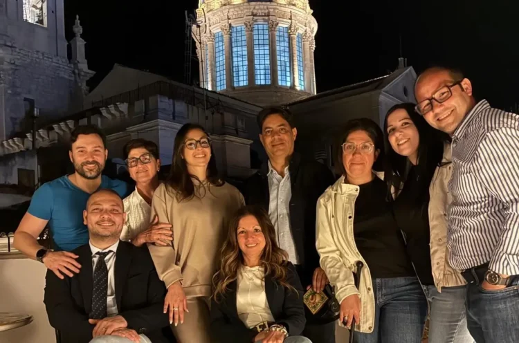 Componenti del gruppo consiliare IdeAzione posano in una foto di gruppo in piazza a Comiso, con la cupola della chiesa illuminata sullo sfondo durante una serata.